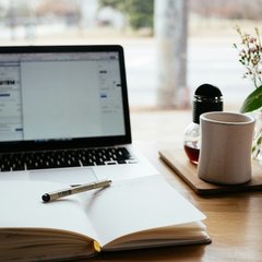 A writing desk with a laptop, notebook, mug, and flowers